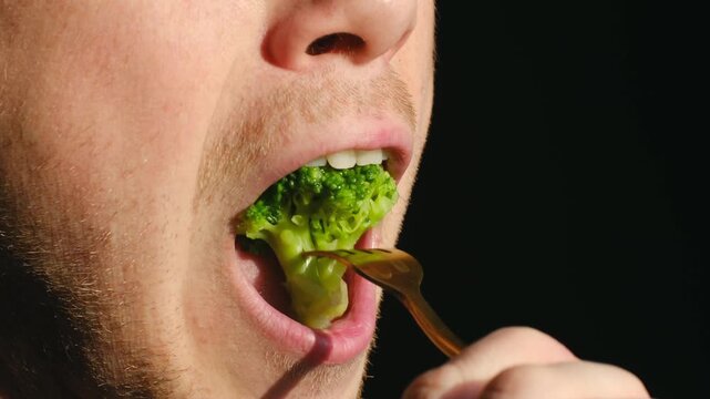 Caucasian man savoring green bites, Profile of man eating healthy vegetables thoughtfully, Portrait of man delicately savoring green vegetable in dark studio setting during contemplative moment