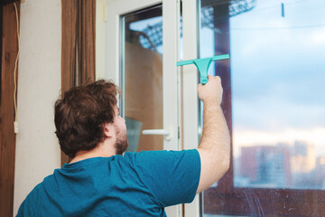 A Caucasian bearded young man washes the window in the kitchen.