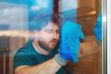 A Caucasian bearded young man washes the window in the kitchen.