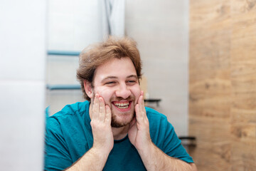 A bearded Caucasian young man washes his face in the bathroom.