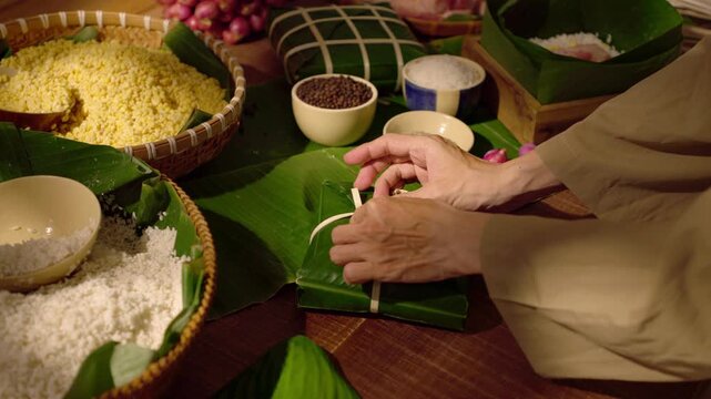 Hands carefully folding dong leaves around sticky rice, showing a precise wrapping step in making banh chung for Vietnamese Lunar New Year