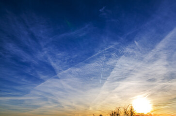 Vast blue sky filled with wispy clouds and airplane contrails during sunset