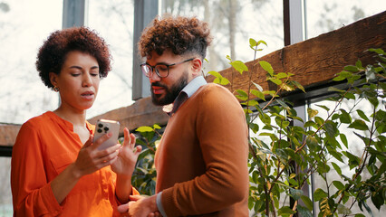 Two colleagues standing in modern office, actively discussing project using smartphone