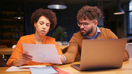 Businesswoman and businessman working together in modern office, analyzing documents, using laptop