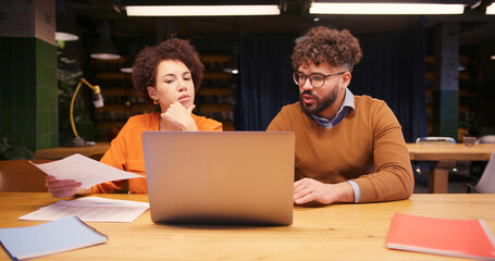 Businesswoman and businessman working together in modern office, analyzing documents, using laptop