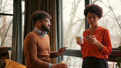 Middle eastern man and African American woman talking together drinking coffee, using mobile app