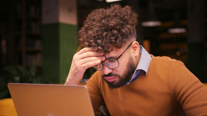Sad male middle eastern worker, programmer working on laptop in modern coworking