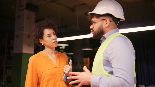 Male project manager discussing building plan with female engineer in hard hat and safety vest