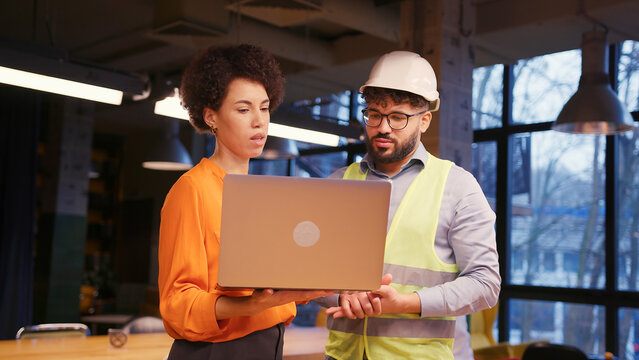 Female architect and male builder in hard hat reviewing building planning on laptop business concept - Powered by Adobe