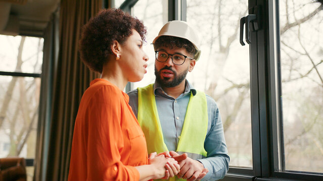 Professional female architect and male builder in hard hat reviewing building talking, analyzing - Powered by Adobe