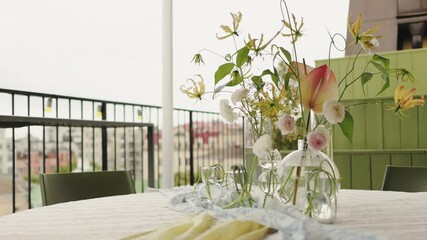 wide terrace table with glass vases and flowing greenery, event planner setting centerpieces against city