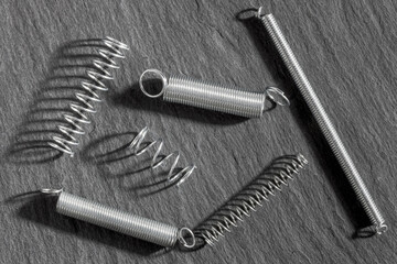 Assorted metallic tension springs arranged on a dark slate background, ideal for industrial,...
