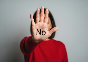 Woman showing stop gesture with word “No” written on palm. Concept of refusal, boundaries, rejection, protest, consent awareness, personal rights and saying no