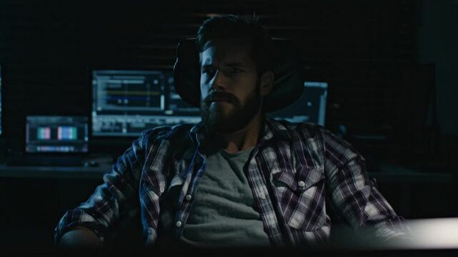 Focused Hacker Working on Computer in Dark Room with Multiple Screens Displaying Code and Data.