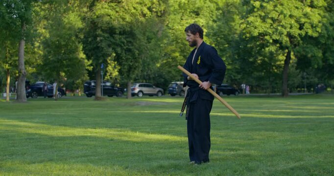 One karateka practices katana strikes. A male karateka trains on the grass with nunchaku and tonfa.