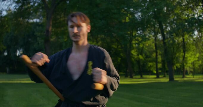 Male karateka practicing precision movements with tonfu. A male karateka trains on the grass with nunchaku and tonfa.