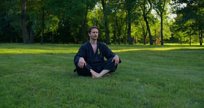 Young karateka catching his breath while sitting on the grass after training. A male karateka trains on the grass with nunchaku and tonfa.
