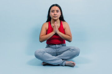 young latina teenager girl doing yoga or meditation with copy space on blue background in Mexico Latin America, Hispanic brunette woman