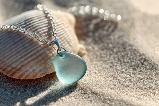 Artisanal sea glass necklace on a seashell with cool blue tones and shimmering chain