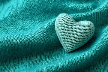 A knitted heart, a symbol of love, rests gently on a soft teal fabric with rich texture. This cozy textile background creates a warm, inviting detail.