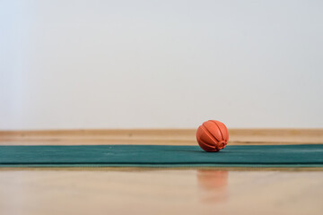 Small orange massage ball for trigger points lying on mat. Small orange massage ball on green mat indoors, tool for fitness training or muscle relaxation.