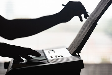 Silhouette of man playing music on piano keyboard, closeup photo. Close-up silhouette of hand writing sheet music while playing piano