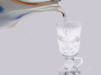 stream of water flows from a jug into a glass on a white background
