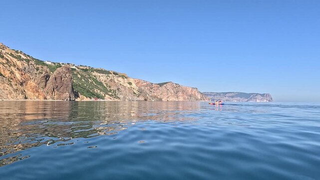 Kayaks sea coastline, two small boats float on calm water near scenic cliffs on a clear summer day