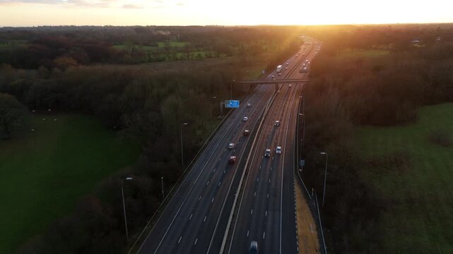 Aerial view of a motorway with vehicles in motion cutting through a landscape of greens and browns at sunset, Solihull, England, United Kingdom.