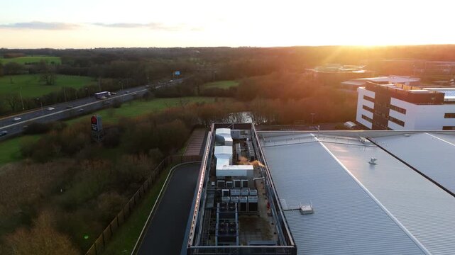 Aerial view of buildings and a highway with vehicles, set against a backdrop of green fields and a radiant sunset, Solihull, England, United Kingdom.