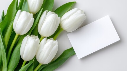 White tulips arranged elegantly on a soft surface with a blank card nearby, creating a serene and fresh atmosphere for greeting or invitation design mock up