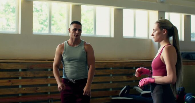 A female mixed martial artist and her coach warm up before MMA training. A female mixed fighter wraps training bandages around her wrists.