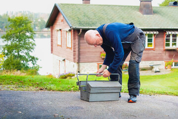 Hands on preparation for task as older man opening a metal toolbox outdoors, focused movement and practical routine showing readiness for manual work.