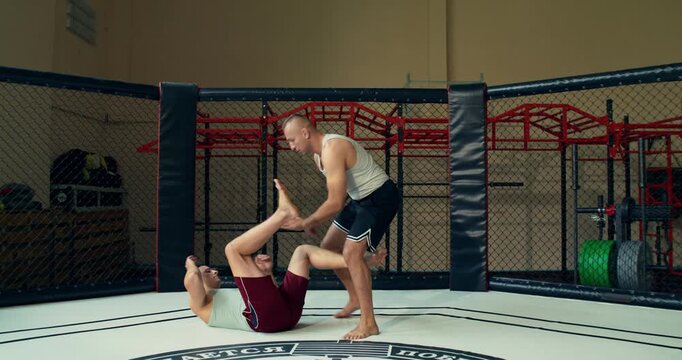 A male coach shows a mixed martial artist takedown technique. One man trains another in the ring.