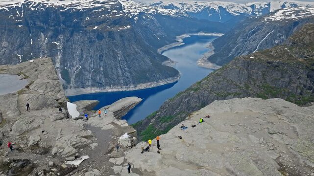 Tourists walking on rocky plateau near Trolltunga above Ringedalsvatnet in Norway. Hikers explore dramatic fjord scenery during an active mountain adventure.