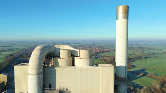 Aerial view of an industrial plant with tall chimneys expelling smoke, contrasted by a row of parked cars near Lawford Road, Rugby, England, United Kingdom.