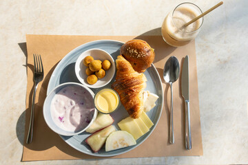 Top view of a hotel breakfast with croissant, yogurt, fruit, cheese, and coffee. Natural light and...