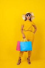 happy young Asian woman in yellow jumpsuit and straw hat jumping for joy on isolated yellow background, summer vacation, fashion travel and energy lifestyle concept.