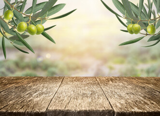 Fresh olive branch and rustic wooden table with copy space for product display over blurred landscape. Background for advertising and placement of natural and organic mediterranean food and oil