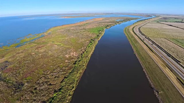 Aerial view of Lake Okeechobee's dark waters contrasting with the adjacent marshland and a ribbon of highway under a clear sky, Lake Okeechobee, Florida, United States.