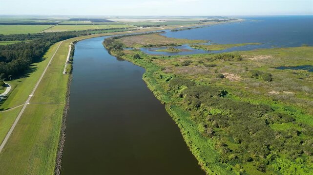 Aerial view of the dark water channel meeting the vast blue expanse of Lake Okeechobee, fringed by lush green vegetation, Lake Okeechobee, Florida, United States.