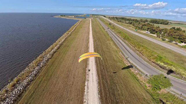 Aerial view of a paraglider soaring over the grassy banks of Lake Okeechobee contrasting with the blue water and sky, Lake Okeechobee, Florida, United States.