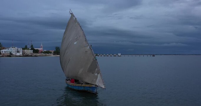 Aerial view of a dhow sailing on tranquil waters, with the historical Ilha de Mocambique coastline in the background, Nampula Province, Mozambique.