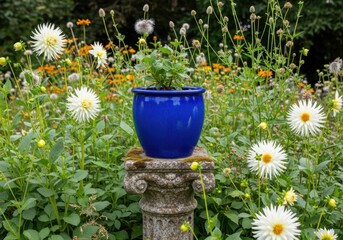 A striking blue pot holding a green plant sits atop an ornate stone pedestal, surrounded by a lush garden filled with white and orange dahlias