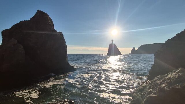 Seascape rocks waves at sunrise casting a lens flare over water near St George's Rock Vertical video