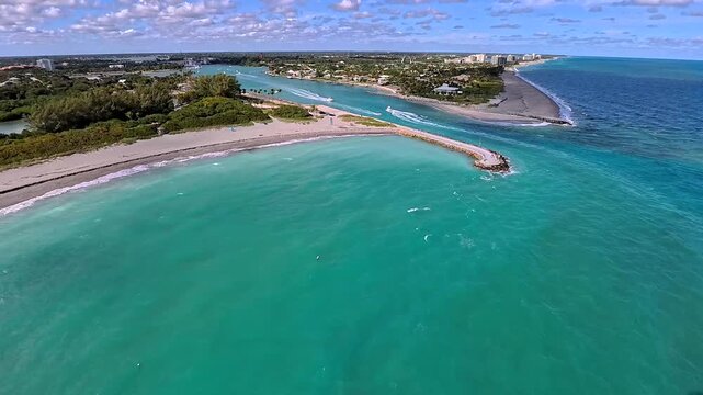 Aerial view of the turquoise inlet where boats pass, with the beach and buildings contrasting against the blue waters, Jupiter Beach, Florida, United States.