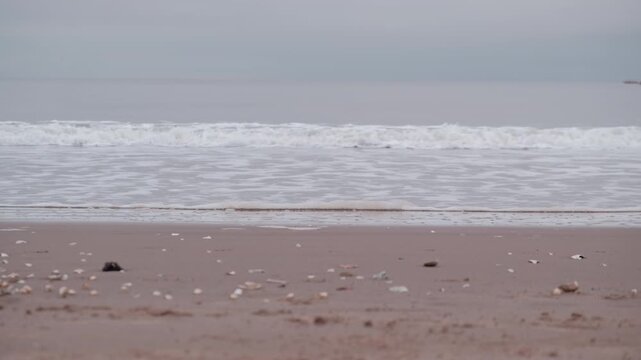 EDINBURGH, SCOTLAND, UK - JANUARY 5, 2024: Portobello Beach during a cloudy sunrise, featuring soft waves, tranquil shore and rowing boat on horizon.
