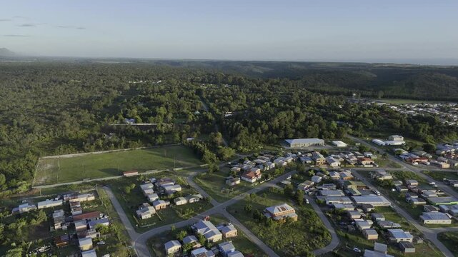 Drone orbits to the right over township outside a forested community at base of the Tsitsikamma Mountains at sunset in Stormsrivier, Eastern Cape, South Africa
