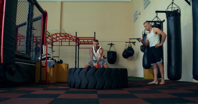 One male mixed martial artist counts the number of sledgehammer strikes to a tire made by the second fighter .