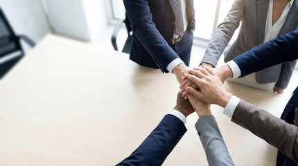 Business team stacking hands together symbolizing teamwork collaboration trust and corporate unity in boardroom with copy space.
